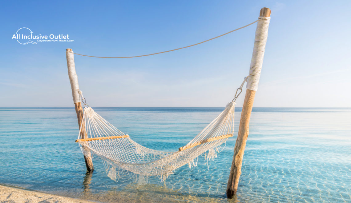 Hammock hanging over crystal clear waters with the All Inclusive Outlet logo